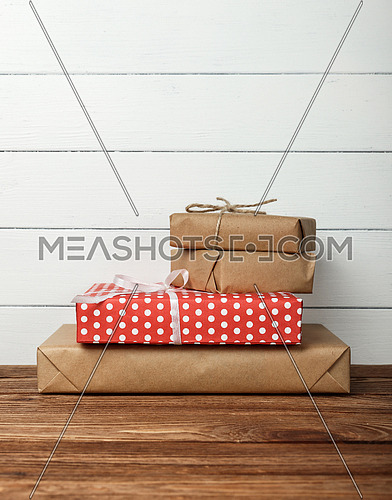 Close up stack of several red and brown paper wrapped gifts on wooden table over white wall