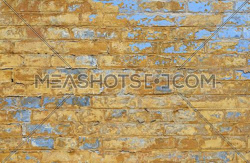 Old grunge vintage yellow painted brick wall with blue paint scale, stains and dirt faded background