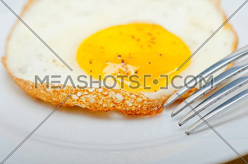 fried egg sunny side up on a plate with fork over wood table