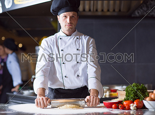 chef preparing dough for pizza rolling with rolling pin on sprinkled with flour table
