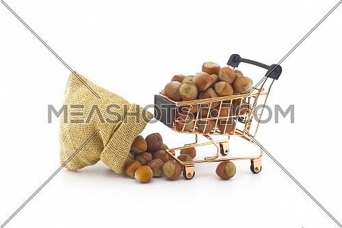 Small hessian bag and shopping cart filled with whole ripe hazelnuts spilling onto a white background