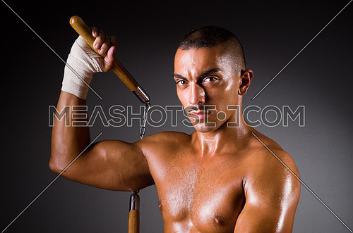 Muscular man with nunchucks on a dark background