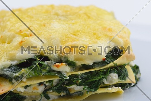 Close-up of a traditional lasagna made with minced beef bolognese sauce topped with basil leafs served on a white plate
