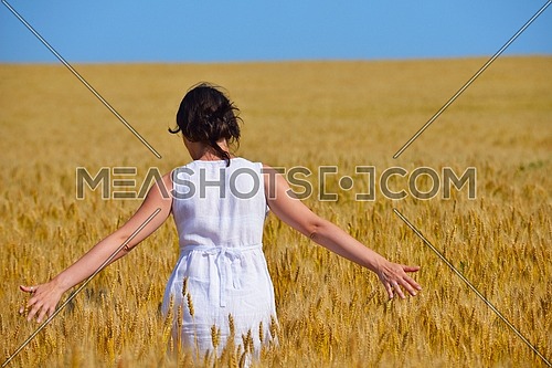 Young woman standing jumping and running  on a wheat field with blue sky the background at summer day representing healthy life and agriculture concept