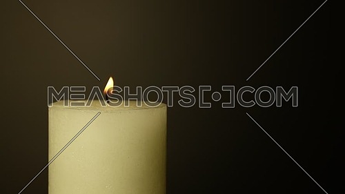 Close up one white candle trembling flame out of the dark over black background, off-center, fired up with lighter, burning and blown out