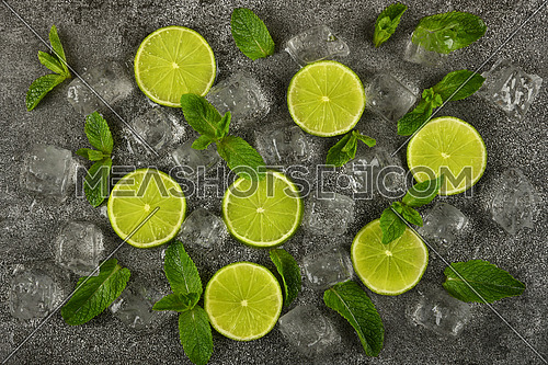 Close up flat lay of lime slices, fresh green mint leaves and ice cubes on grunge gray stone table surface, elevated top view, directly above