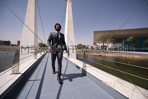 young middle eastern  businessman walking across modern bridge