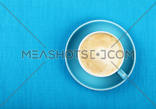 Full cup of latte cappuccino coffee with milk froth on saucer over blue tablecloth, close up, elevated top view