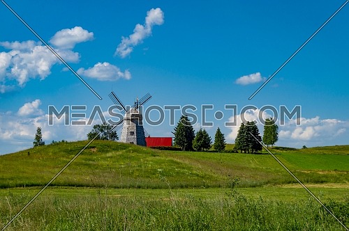 Historic windmill in a lush green field against a sunny blue sky and white clouds in a scenic landscape