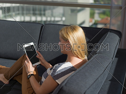 beautiful young woman on sofa at home surfing  internet using tablet computer