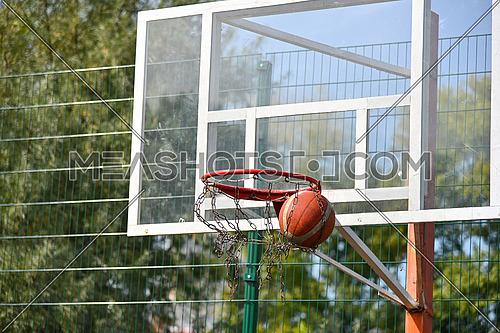 Close up shooting orange colored basketball ball into the basket at outdoors court, low angle, front view
