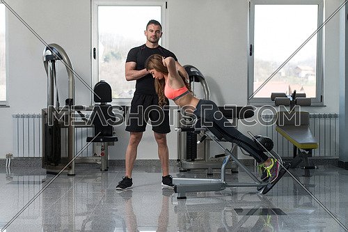 Personal Trainer Showing Young Woman How To Train Back On Machine In The Gym