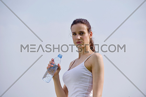 Young beautiful woman drinking water after fitness exercise and jogging outdoors