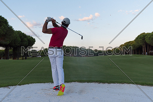 golf player shot ball from sand bunker at course with beautiful sunset with sun flare