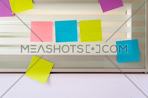 Randomly scattered colored sticky notes over glass screen of a bench desk