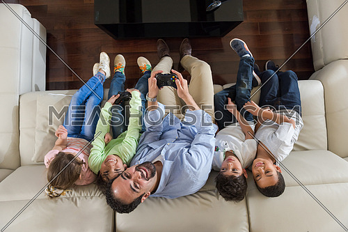 middle eastern man enjoys playing video games with the kids on the sofa