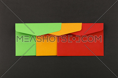 Close up group of three colorful mail envelopes, green, yellow and red, over grey paper background, elevated top view, directly above