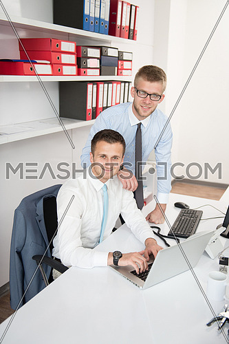 Two Businessmen In An Office Smiling At The Camera While Working Together Behind A Laptop Computer
