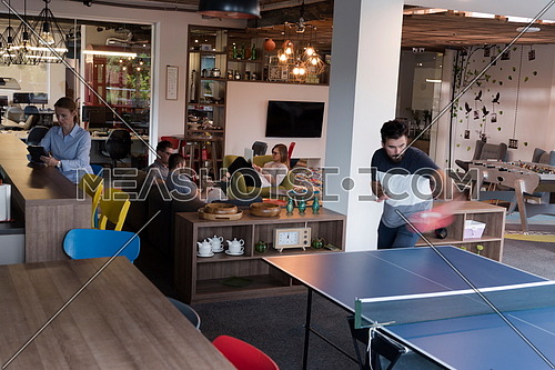 Two young start up business man playing ping pong tennis at modern creative office space  people group have meeting and brainstorming in background