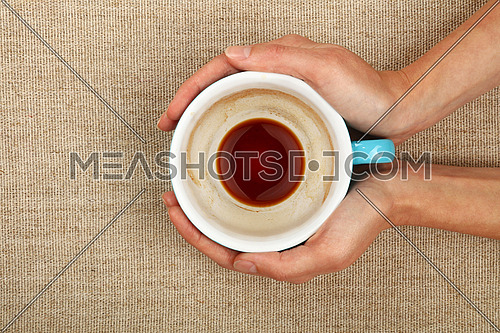Two woman hands holding embracing big empty finished black coffee blue cup over linen canvas background