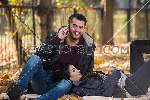Beautiful Young Couple Sitting In The Park On A Beautiful Autumn Day - Boyfriend Using A Telephone