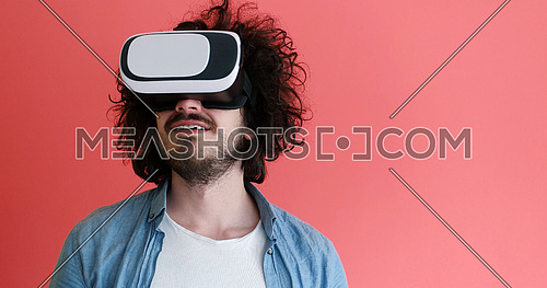 Happy man getting experience using VR headset glasses of virtual reality, isolated on red background