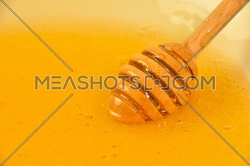 Close up wooden honey dipper spoon in bowl of fresh thick fluid acacia honey, high angle view
