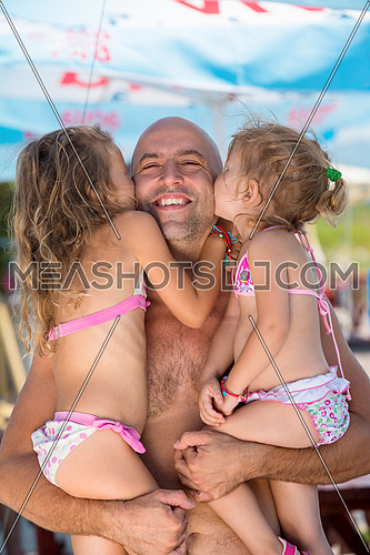 portrait of young happy father having fun with his cute little daughters while holding them in his hands by the sea during Summer vacation  Healthy family holiday concept