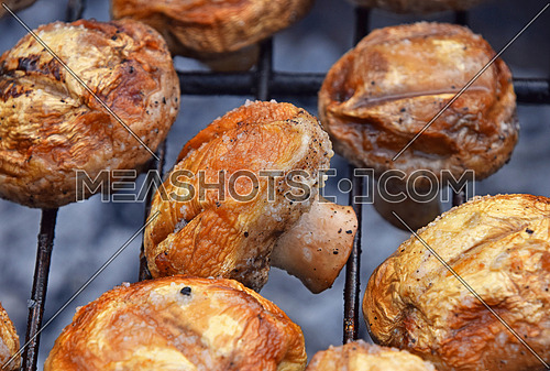 White champignons portobello mushrooms being cooked on char grill, close up