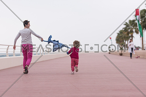 young mother and cute little girl running and cheerfully spend their time on the promenade by the sea