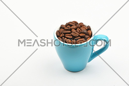 One small blue espresso cup full of roasted coffee beans over white background, close up, high angle view, personal perspective