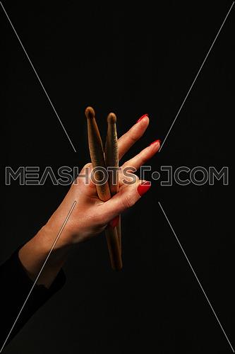 Woman hand holding two drumsticks with devil horns rock metal gesture sign over black background, side view