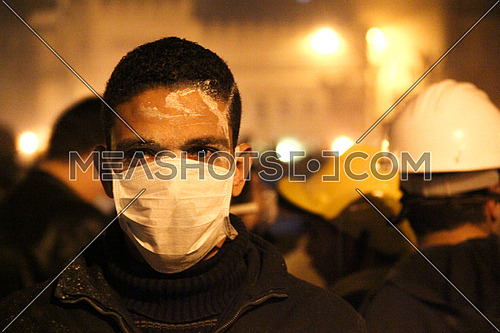 a man wearing a mask and looking to camera during a protest at night