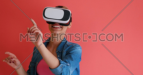 Happy girl getting experience using VR headset glasses of virtual reality, isolated on red background