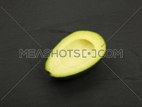 One fresh ripe green avocado half with pit stone on black slate board background, detail, close up, high angle view