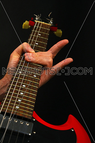 Male hand holding red sg guitar neck with devil horns rock metal sign isolated on black background