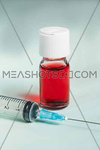medical vaccine vials with red liquid and syringe over green table and white background. Vaccination and immunization conceptual.