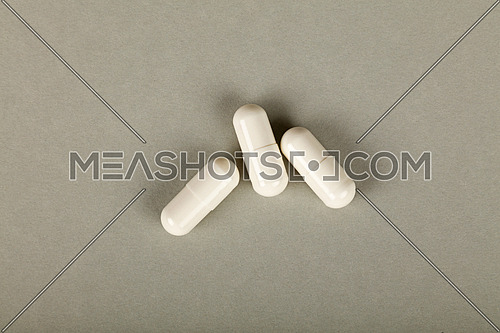 Close up three white gel cap pills of medicine over grey background with copy space, elevated high angle view, directly above