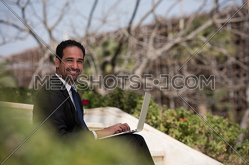 Handsome business executive sitting on stairs if a corporate building working on laptop