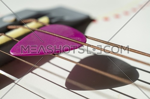 Colorful pink plectrum in guitar strings in a close up oblique angle view in a music and entertainment concept