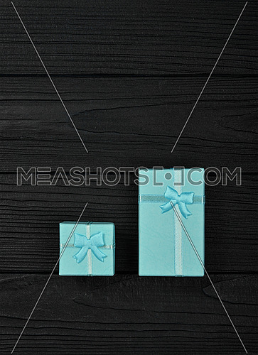 Valentine template of two closed small blue gift boxes with ribbon bows over black wooden table background, close up flat lay, elevated top view, directly above