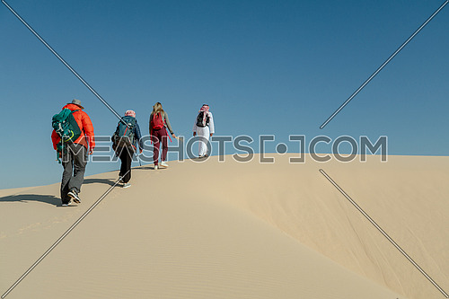 Group of tourists walking on sands with bedouin guide while exploring Sinai Trail from Ain Hodouda by day.