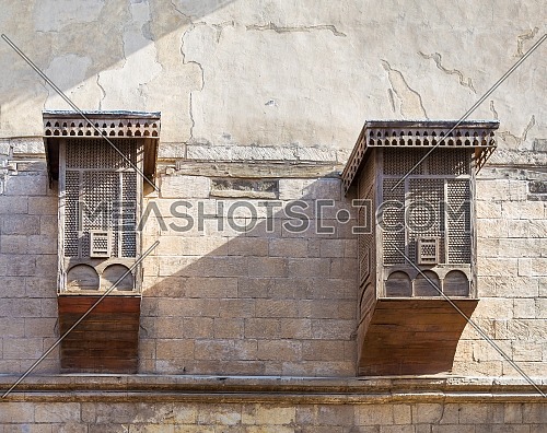 Two Mamluk era style oriel windows covered by interleaved wooden grid (Mashrabiya), on shabby grunge external wall, old Cairo, Egypt