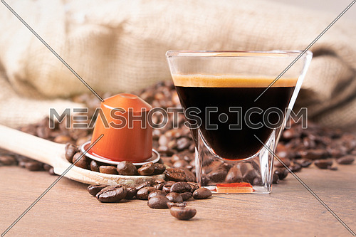 Cup of coffee with coffee capsule on wooden spoon, roasted coffee beans on wooden background,front view.