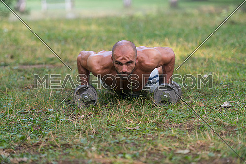 Young Muscular Athlete Doing Push Ups With Dumbbells As Part Of Bodybuilding Training - Outdoors Workout - Sports And Fitness - Concept Of Healthy Lifestyle - Fitness Male