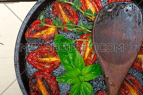oven baked cherry tomatoes with basil and  thyme on a cast iron skillet and wood spoon