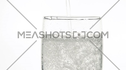Close up of pouring pure clear sparkling water with gas in transparent glass until full over white background, low angle side view, slow motion