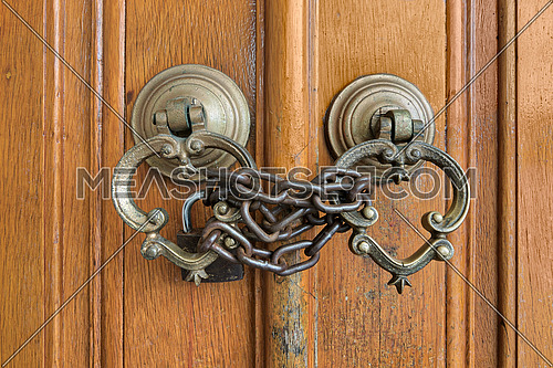 Closeup of two antique copper ornate door knockers over an aged wooden ornate door closed with rusted chain and padlock, Eyup Sultan Mosque, Istanbul, Turkey