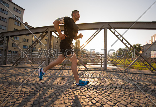 young sporty man jogging across the bridge at sunny morning in the city