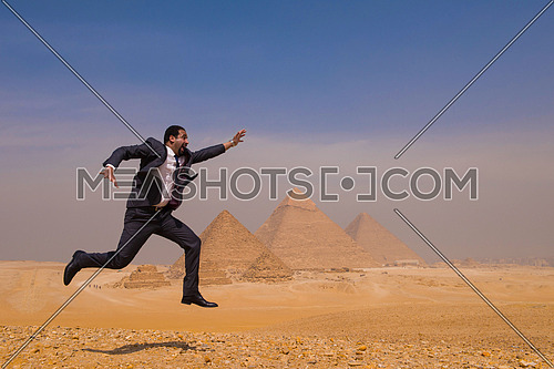 Egyptian business man jumping in desert with pyramids in background
